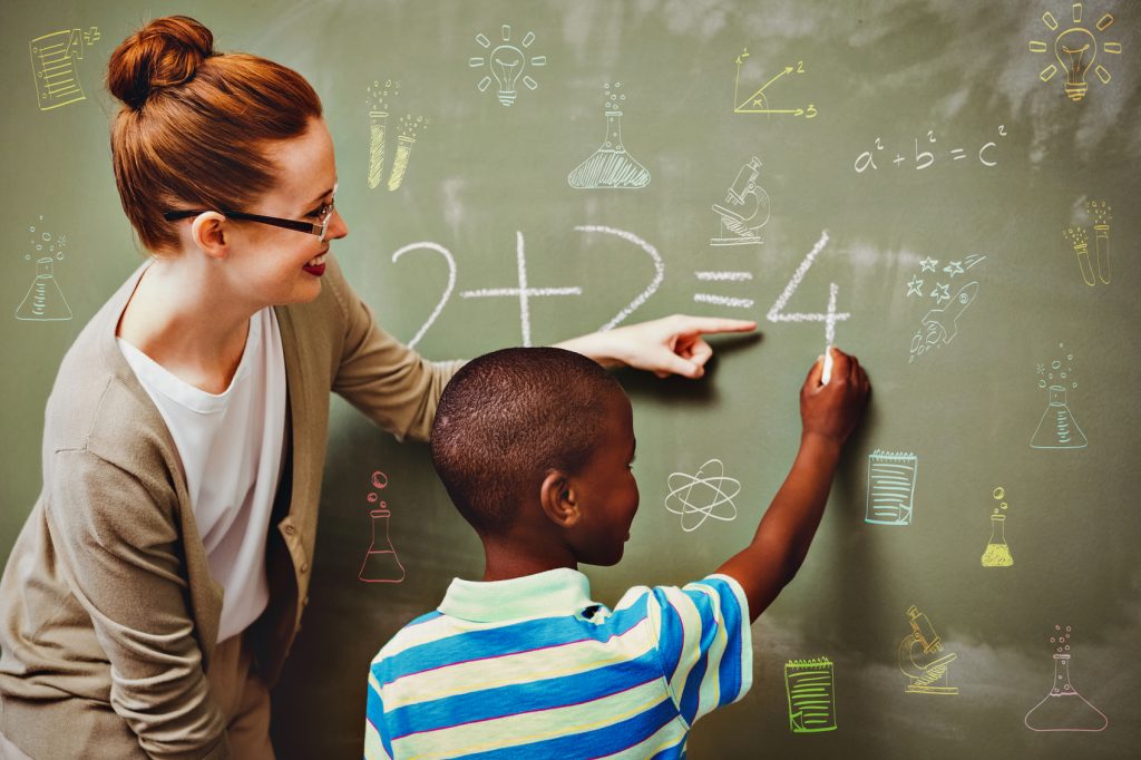 School subjects doodles against teacher assisting boy to write on blackboard in classroom